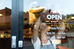 A woman hangs an open sign on the window of her storefront. Glass Speciality WLC installs and repairs Commercial Glass in Galesburg IL.