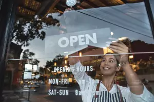 A woman turns a sign to "open" on her store window. Glass Specialty WLC installs Commercial Glass in Monmouth IL