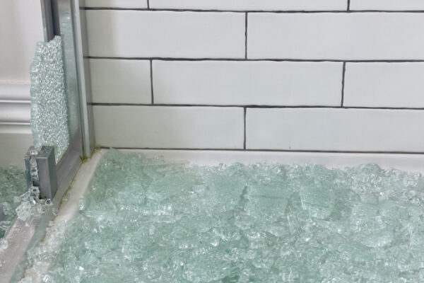 Shower Enclosures Kewanee IL, A pile of tempered safety glass chips on the floor of a tiled bathroom next to a metal shower door frame